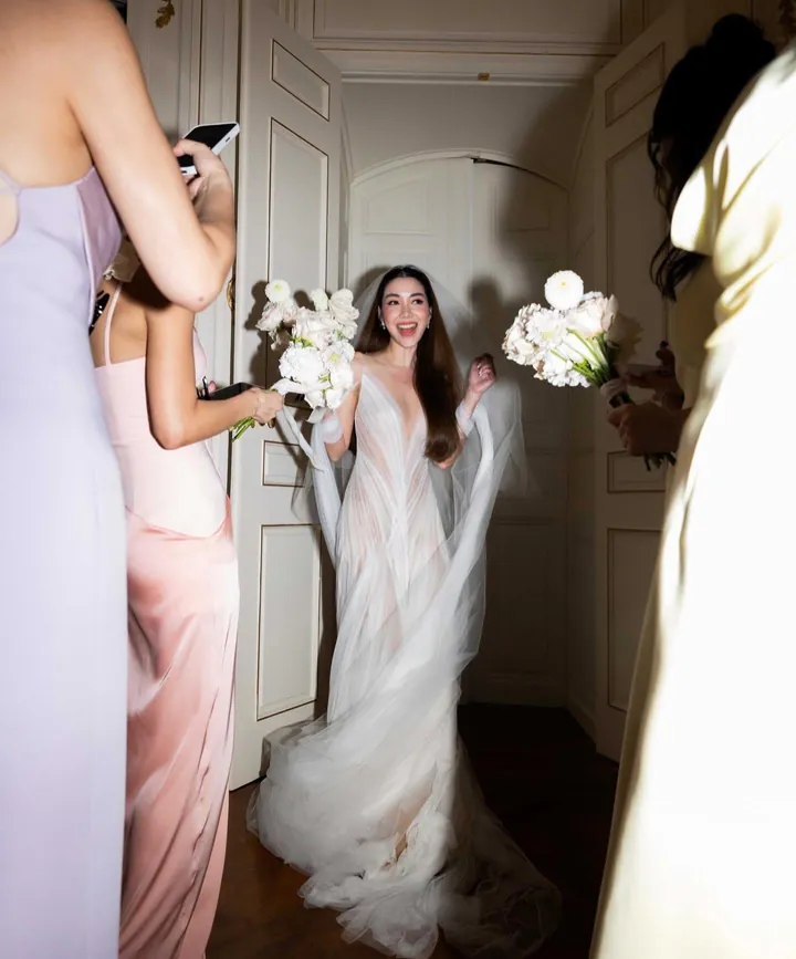 A laughing bride in a plunging tulle gown in a doorway, her bridesmaids in pink and lilac holding white bouquets