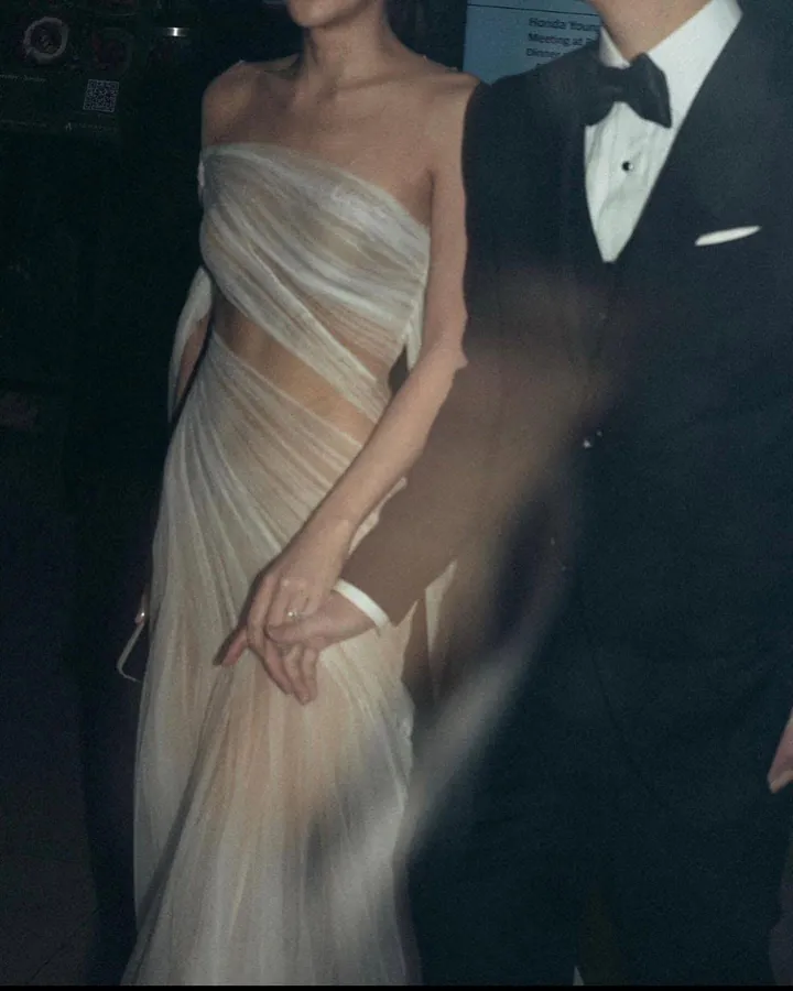 A bride holding hands with her groom, her strapless gown of draped champagne tulle wrapping the body