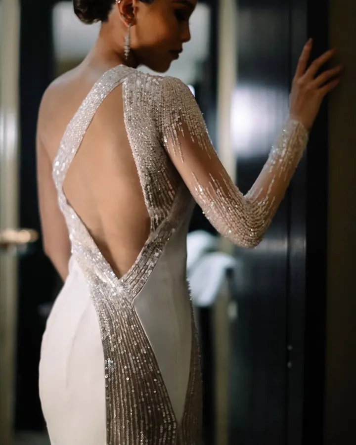 A bride by a doorway, her gown's open back framed with lines of crystal beading