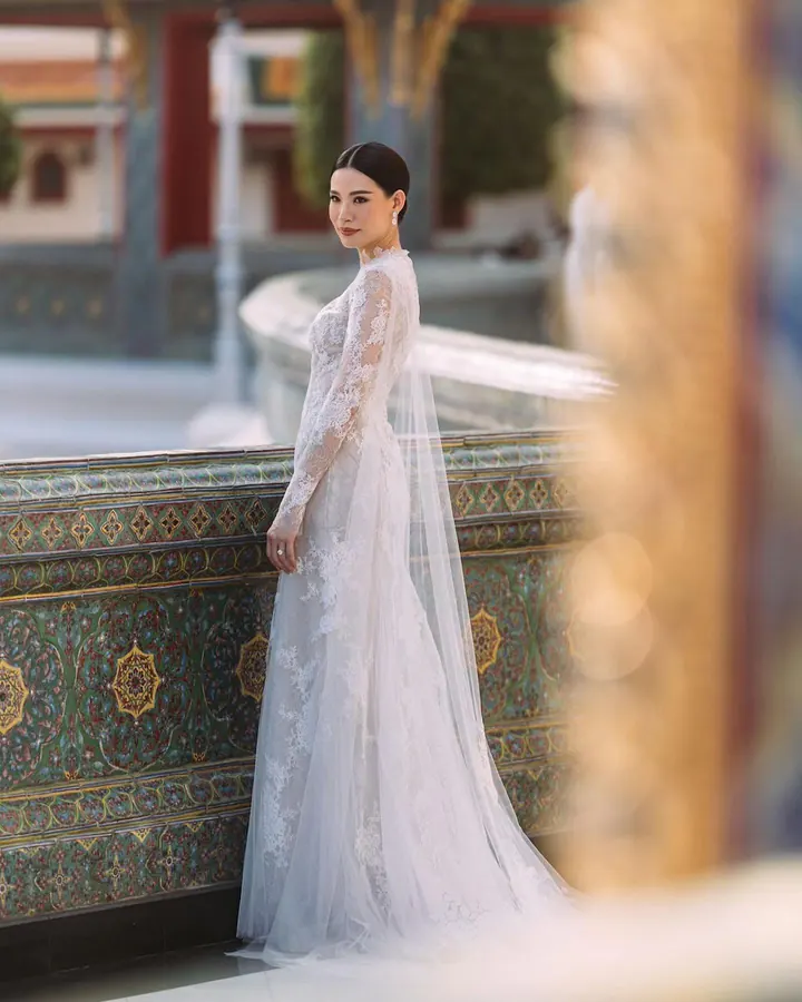 A bride in a long-sleeved lace gown and veil beside a tiled balustrade