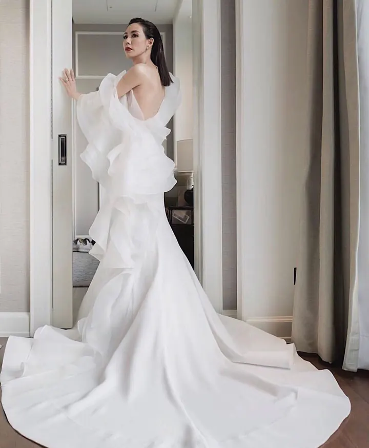A bride in a satin mermaid gown with a sculpted ruffle at the back and a wide pooled train