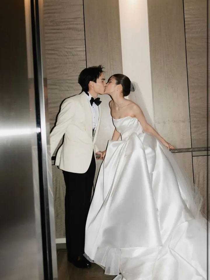 A groom kissing a bride in a strapless satin ball gown in a hotel lift