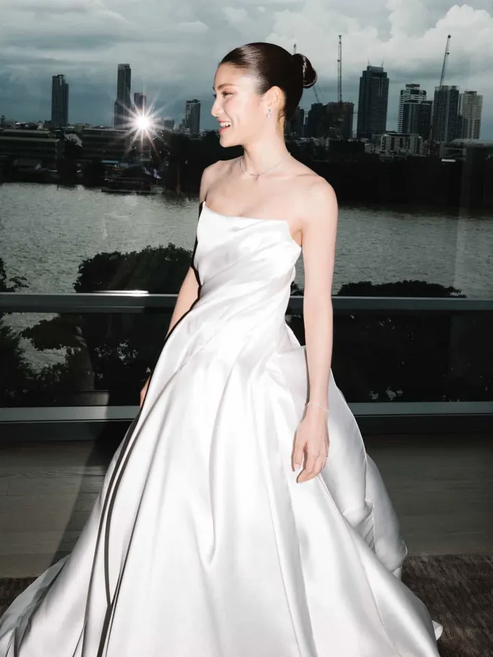 A bride in a strapless structured satin gown on a riverside balcony with the Bangkok skyline behind