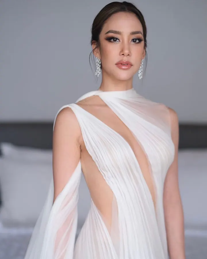 A bride in an asymmetric, sculpted gown with sheer panels and a draped sash over one shoulder