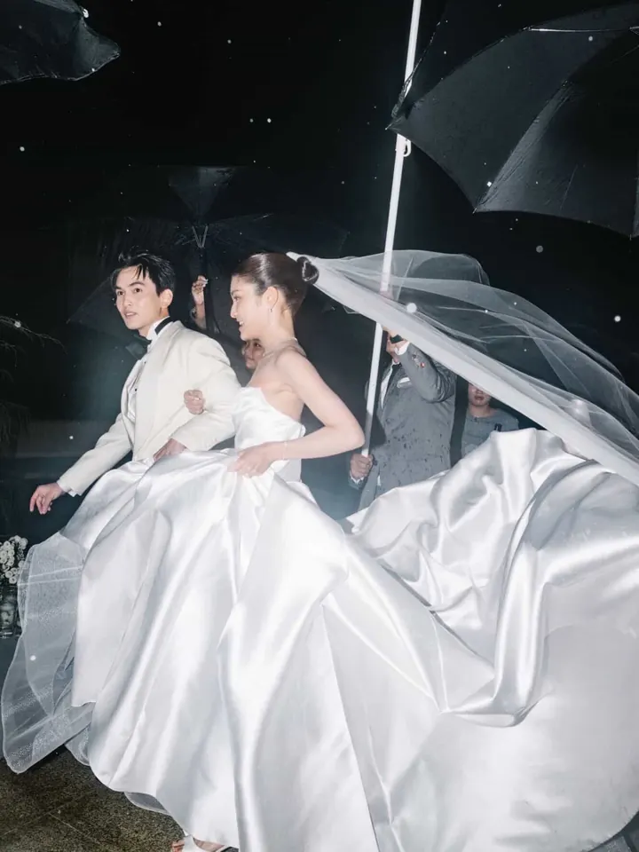 A bride and groom running under umbrellas at night, her satin skirt billowing