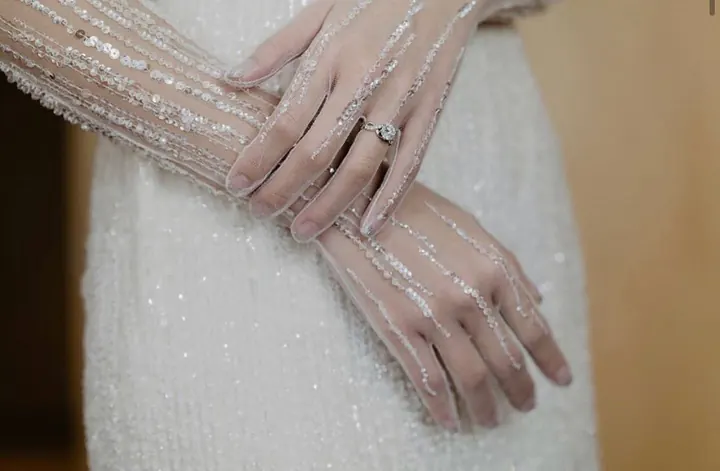 Close-up of hands resting on a skirt, the sheer sleeves embroidered with lines of beading