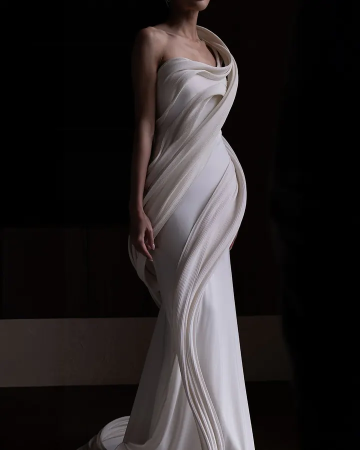 A Patarasiri gown of sculpted, hand-draped ivory fabric spiralling around the body, lit against black