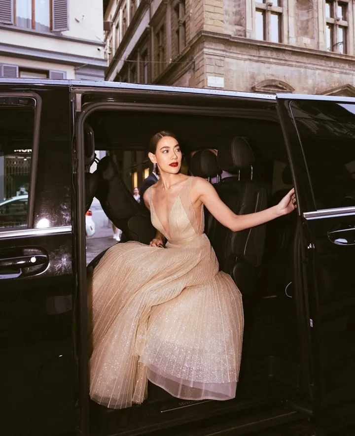 A woman stepping out of a car in a champagne tulle gown with a plunging neckline