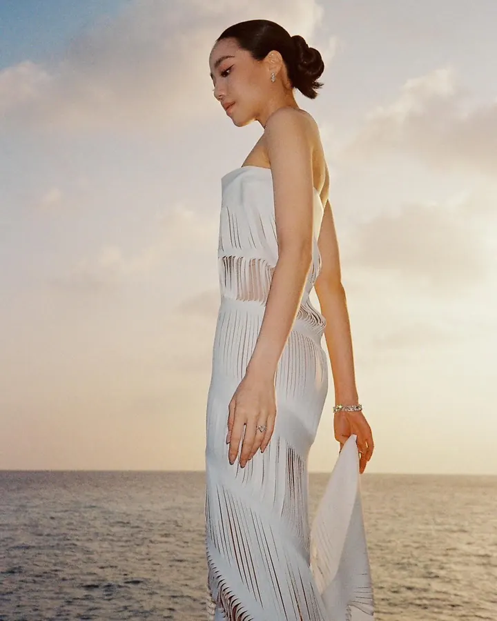 A woman by the sea at sunset in an ivory dress of sculpted, cut-work bands