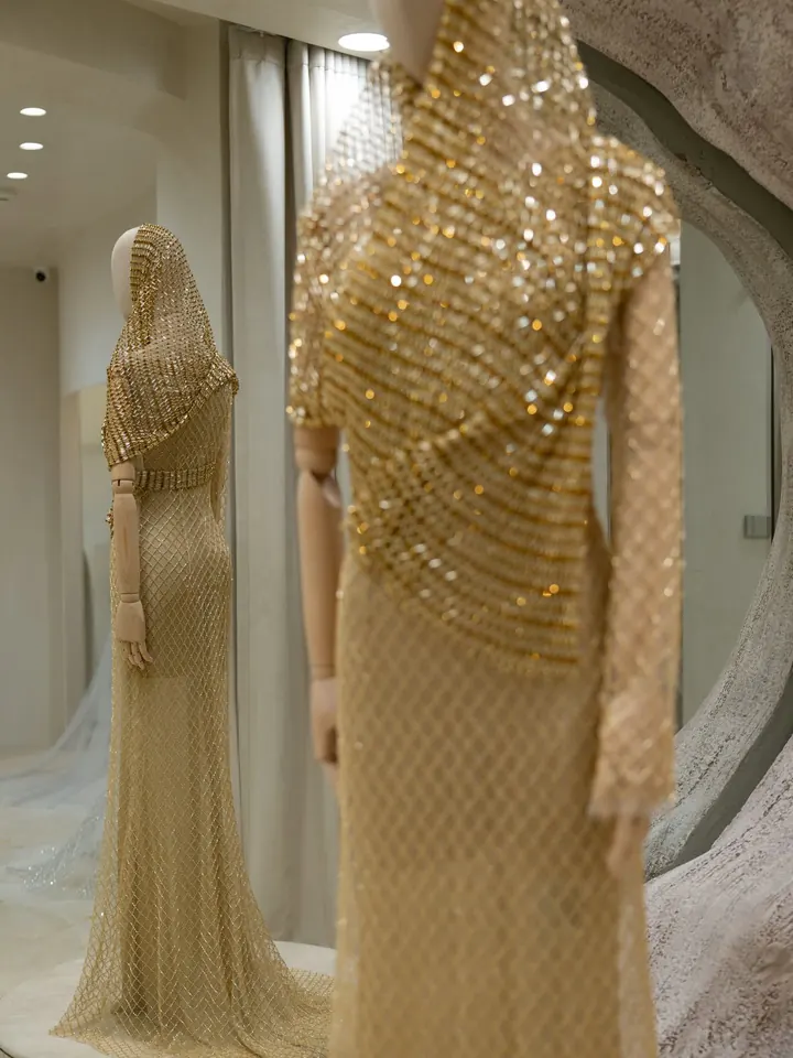 Two Patarasiri Regalia pieces on dress forms in the atelier, covered in gold sequins and latticed beading